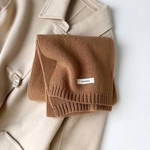 Dettaglio della sciarpa in lana color caramello con etichetta 100% lana su cappotto beige