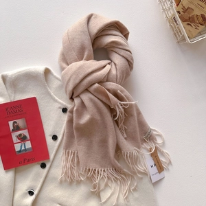 Détail d'une écharpe pashmina beige avec franges et étiquette de marque sur un manteau blanc