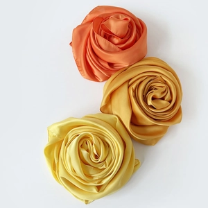 Detalle de bufandas de satén dobladas en forma de rosa en naranja, dorado y amarillo