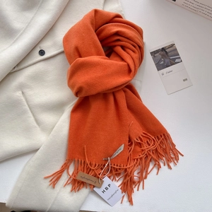 Détail de l'écharpe orange vif avec franges et étiquette sur fond de manteau en laine blanc