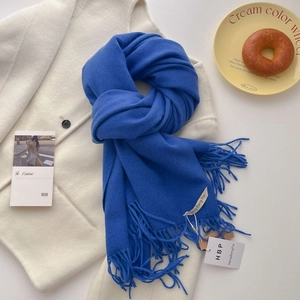 Détail d'une écharpe bleue effet cachemire avec franges sur un manteau blanc chic