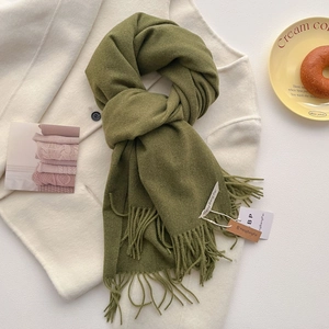 Détail d'une écharpe vert foncé à franges sur fond de manteau en laine beige