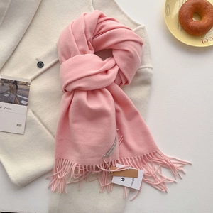 Vue détaillée d'une écharpe en cachemire rose doux avec franges sur manteau blanc