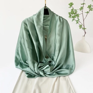 Detalle de chal de seda satinada verde menta con acabado brillante colgado en percha