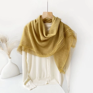Detail of ginger yellow linen shawl with delicate lace edges on a white hanger