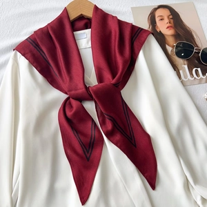 Detail of burgundy herringbone silk scarf with black V-stripe trim on a hanger