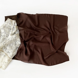 Detail shot of elegant dark brown satin fabric paired with intricate white floral lace texture