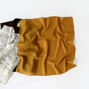 Detail of mustard yellow square silk scarf showing smooth texture and elegant drape