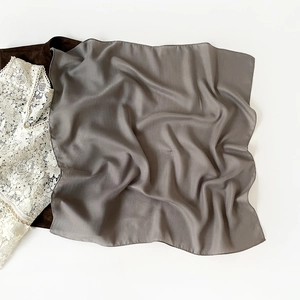 Detail of dark grey silk square scarf with glossy texture draped on lace shirt