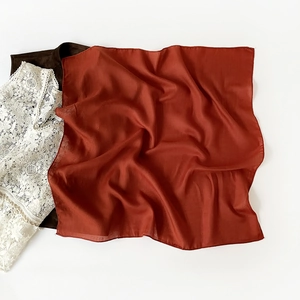 Detail of rust red satin square scarf showing smooth texture and elegant drape over lace