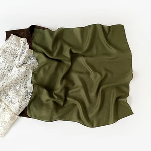 Detailed close-up of dark green silk satin scarf textured against lace shirt fabric