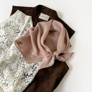 Close-up of pink silk scarf with herringbone texture paired with a brown suede vest