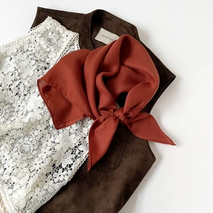 Detail view of rust red silk scarf tied in a bow with elegant herringbone twill texture