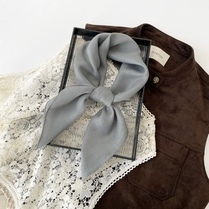 Close-up of light gray silk scarf featuring delicate herringbone texture and elegant bow knot