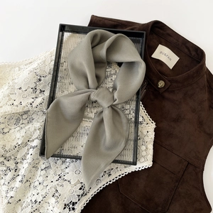 Detail showing the gray-green silk scarf tied in a neat bow with fine diagonal textures
