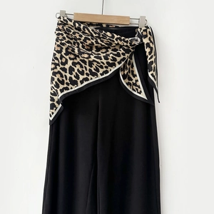 Detail of a leopard print silk scarf tied as a stylish belt on black wide leg trousers