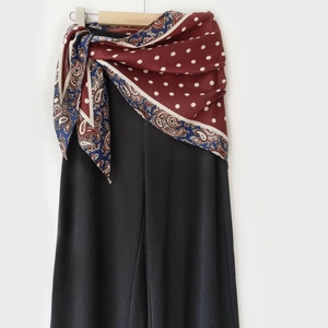 Détail d'un foulard en soie bordeaux noué sur un pantalon noir à jambes larges