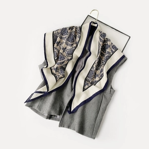 Détail d'un foulard en soie à motif damassé porté sur un gilet gris sur cintre