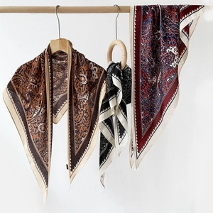 Détail de foulards triangle cachemire en marron, noir et rouge sur cintres en bois