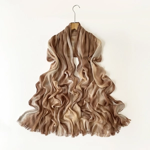 Detail of gradient brown pleated shawl with fine fringe hanging on a wooden hanger