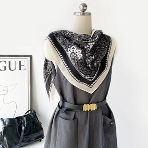Détail d'un foulard en soie à motif paisley porté sur une robe grise avec ceinture chic