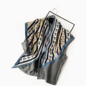 Detail of printed silk scarf with horse pattern draped on a grey vest against white background