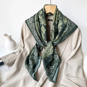 Detail shot of green paisley silk scarf tied over a beige blazer in chic lifestyle setting