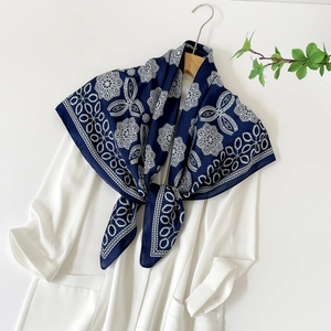 Close-up of a navy blue satin square scarf with white floral print on a wooden hanger