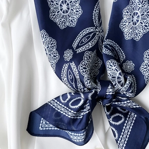 Detailed macro view of smooth dark blue silk scarf with white lace print in a bow knot