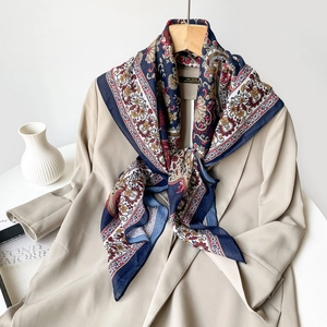 Detailed view of a navy blue paisley silk scarf styled with a beige classic trench coat