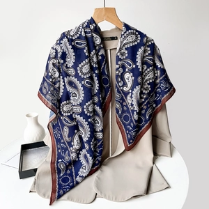 Close-up of navy paisley silk scarf draped on a beige blazer with intricate border detail