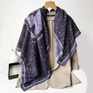 Detail shot of purple paisley printed silk scarf draped over a beige blazer on a wooden hanger