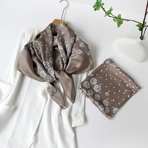 Dettaglio di un foulard di seta caffè con motivi di rose e catene su un blazer bianco