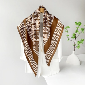 Détail du foulard carré en satin de soie à motif grec marron sur un blazer blanc