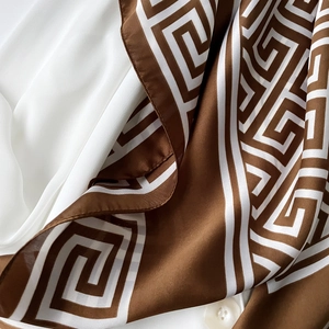 Gros plan d'un foulard en soie marron et blanc avec motif géométrique rétro