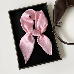 Detail of pink paisley silk scarf tied in a bow on a black display tray with a leather handbag