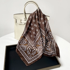 Detailed macro of coffee brown paisley silk scarf draped over a classic handbag