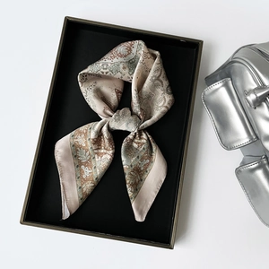 Détail d'un foulard en soie à motif paisley beige et marron dans un coffret cadeau noir