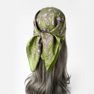 Detailansicht eines grünen Paisley-Seidenschals, gebunden als Boho-Stirnband auf gewelltem Haar