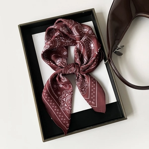 Detail of burgundy paisley silk scarf tied in a bow next to a brown patent handbag