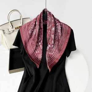 Close-up of a burgundy paisley print silk scarf styled on a black garment for elegance