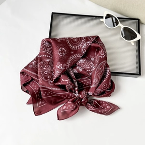 Detail of burgundy paisley satin square scarf tied neatly next to retro sunglasses