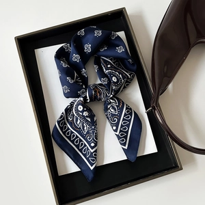 Close-up of a navy blue paisley silk scarf tied in a bow on a white display background