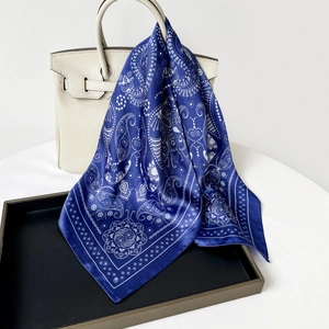 Detailed close-up of dark blue paisley silk scarf draped over a white leather luxury handbag