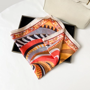 Dettaglio di un foulard in seta con stampa geometrica piegato su un vassoio nero