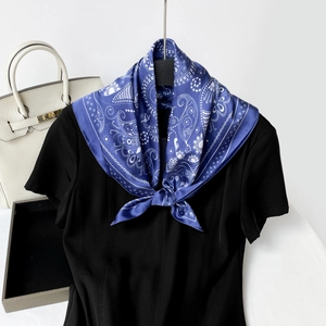 Close-up of a navy blue paisley silk scarf styled on a black dress with a white handbag