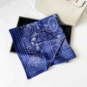 Detail of blue paisley satin scarf with white cashew flower print on a leather handbag