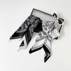 Dettaglio di foulard in raso con motivo paisley su un vassoio con occhiali da sole