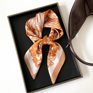 Detailed view of an orange silk-textured square scarf with floral prints and satin finish