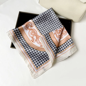 Detail of a silky houndstooth and baroque pattern square scarf on a black tray with a handbag